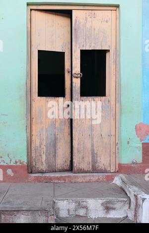249 Faded wood door in beige color of an old house in the Plaza Tres Cruces Square area, on a peeling mint green-maroon-blue facade. Trinidad-Cuba. Stock Photo