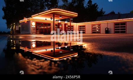 Old beautiful illuminated petrol station on a rainy night with a reflection in a puddle Stock Photo