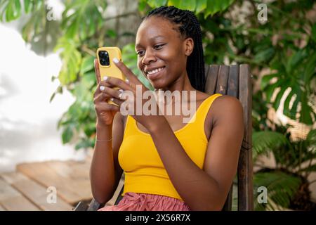 Giggling African American woman using phone. Happy girl relaxing at indoor home urban jungle. Stock Photo