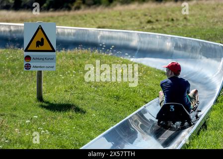 Boy with toboggan on the summer toboggan run, warning sign Attention curve, ski and toboggan arena, Hoherodskopf mountain summit, excursion Stock Photo