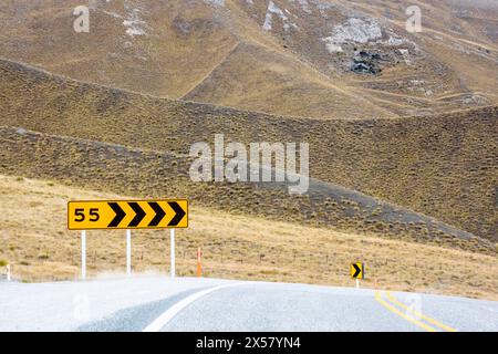 Road through Lindis Pass Alpine Highway,  New Zealand - speed sign of 55km for approaching the corner. Stock Photo