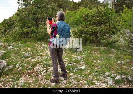 Senior woman standing on the mountain path and taking photo Stock Photo