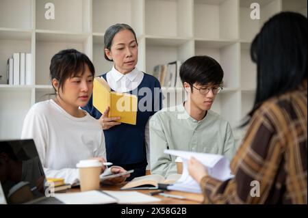 A strict senior Asian female professor or teacher is teaching her students in the classroom. A group of a university students studying with a mature f Stock Photo