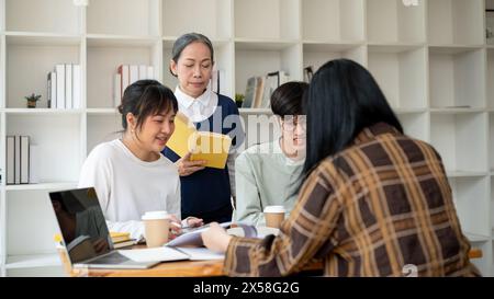 A strict senior Asian female professor or teacher is teaching her students in the classroom. A group of a university students studying with a mature f Stock Photo
