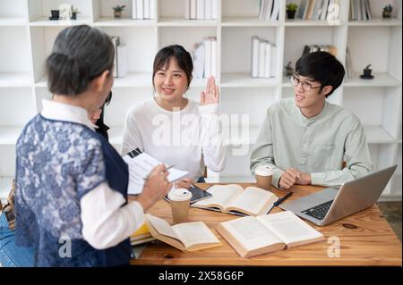 A positive young Asian female university student is raising her hand, asking or answering a question to her professor while studying in the classroom. Stock Photo