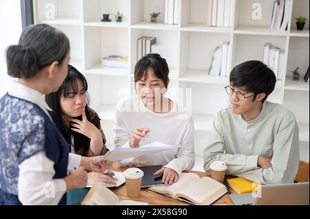 A group of young Asian university students is studying math with a senior professor in the classroom, listening to their professor explain the math pr Stock Photo