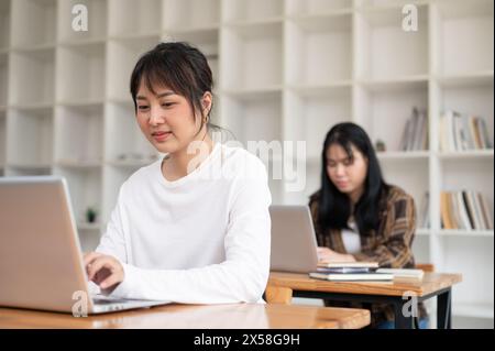 A positive, charming young Asian female university student is using her laptop computer while listening to a teacher lecture in the classroom. Stock Photo