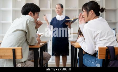 Two young Asian college students are whispering, enjoying talking and ignoring the lesson in the classroom. gossiping, university life, education conc Stock Photo