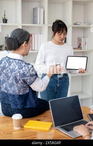 A young Asian female college student is showing her project on her digital tablet, presenting her project in the classroom to her teacher and friends. Stock Photo