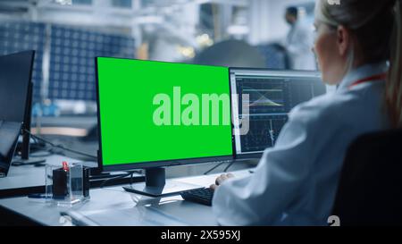 Female Engineer uses Green Screen Computer to Analyse Satellite. Aerospace Agency Manufacturing Facility: Scientists Develop, Assemble Spacecraft for Space Exploration Mission. Over Shoulder Stock Photo