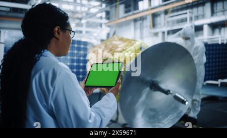 Female Engineer Uses Green Screen Tablet Computer while Working on Satellite Construction. Aerospace Agency: Scientists Assemble and Manufacture Spacecraft for Space Exploroation, Observation Mission Stock Photo