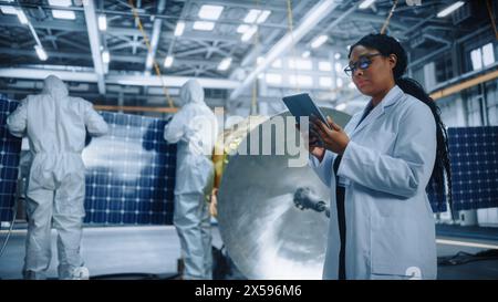Technicians in Protective Suits Working on Satellite Construction, under Chief Engineer Control. Aerospace Agency: Team of Scientists Fixing Solar Panel Wings to Spacecraft. Space Exploration Mission Stock Photo
