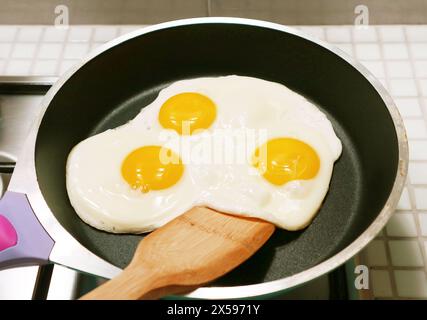 Three of chicken eggs sunny side up being fried in a pan Stock Photo