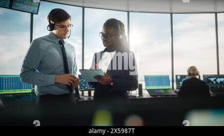 Female and Male Air Traffic Controllers with Headsets Talk in Airport Tower. Office Room is Full of Desktop Computer Displays with Navigation Screens, Airplane Departure and Arrival Data for the Team. Stock Photo
