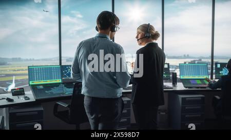 Female and Male Air Traffic Controllers with Headsets Talk in Airport Tower. Office Room is Full of Desktop Computer Displays with Navigation Screens, Airplane Departure and Arrival Data for the Team. Stock Photo