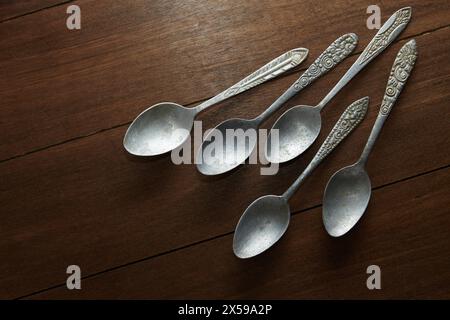 five old spoons made of silver with carved ornaments on the handles with wooden background Stock Photo