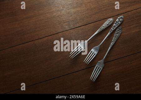 Three old silver forks with ornate carvings on the handles on a wooden motif background Stock Photo