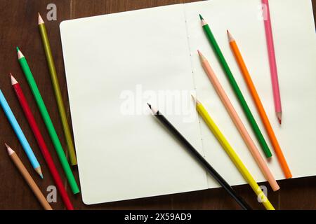 Eleven coloured pencils and an empty sketchbook on a wooden table Stock Photo