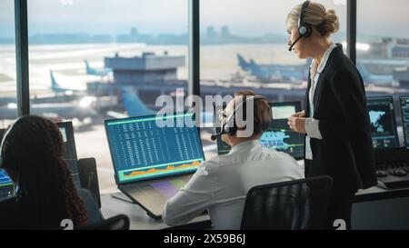 Female and Male Air Traffic Controllers with Headsets Talk in Airport Tower. Office Room is Full of Desktop Computer Displays with Navigation Screens, Airplane Flight Radar Data for the Team. Stock Photo