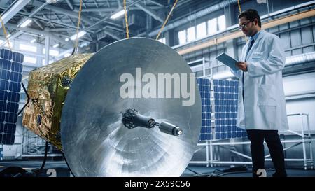 Male Engineer Uses Digital Tablet Computer while Working on Satellite Construction. Aerospace Agency: Scientist Overseeing Building and Assembly of Spacecraft for Space Exploration Mission Stock Photo