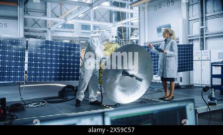 Female Engineer Uses Tablet Computer while Working on Satellite Construction. Aerospace Agency Manufacturing Facility: Scientists Build, Assemble Spacecraft for Space Exploration, Observation Mission Stock Photo