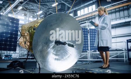 Female Engineer Uses Digital Tablet Computer while Working on Satellite Construction. Aerospace Agency: Scientist Overseeing Building and Assembly of Spacecraft for Space Exploration Mission Stock Photo