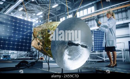 Female Engineer Uses Digital Tablet Computer while Working on Satellite Construction. Aerospace Agency: Scientist uses Augmented Reality Software for Building Spacecraft for Space Exploration Stock Photo
