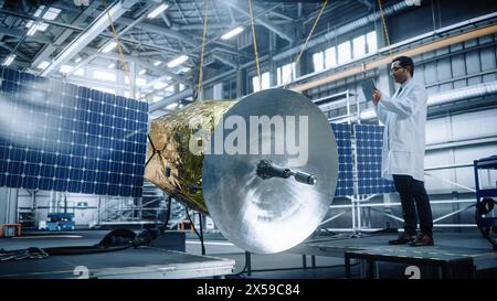 Male Engineer Uses Digital Tablet Computer while Working on Satellite Construction. Aerospace Agency: Scientist uses Augmented Reality Software for Building Spacecraft for Space Exploration Stock Photo