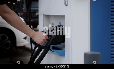 Driver of electric car hold batteries charger plug. Hand holding EV charging plug in front of camera with blurred background of outdoor. Sustainable e Stock Photo