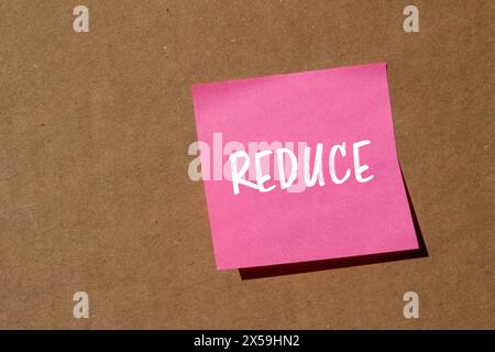 Reduce word written on pink paper sticker with brown background. Conceptual reduce symbol. Copy space. Stock Photo