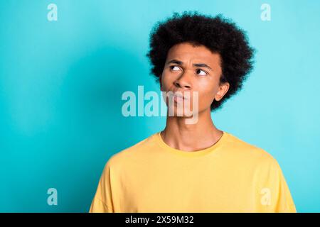 Portrait of minded puzzled man with afro hairstyle wear oversize t-shirt look at offer empty space isolated on teal color background Stock Photo