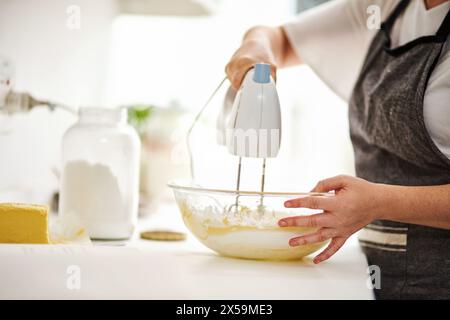 Bowl, hands and mixer for baking with person in kitchen of home closeup for pastry preparation. Batter, cooking and food with baker or chef at counter Stock Photo