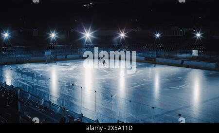 Ice Hockey Rink Arena: Professional Player Training Alone. Skates, Dribbles with Stick, Shooting, Hitting the Puck. Determined Athlete with Desire to Win, Be Champion. Cinematic Lights Stock Photo