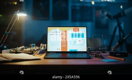 Laptop Computer Standing on a Table with a Science Homework School Project on Robotics on Screen. Cozy Empty Room with a Lamp, Circuit Board, Newton's Cradle and Tools on the Table. Stock Photo