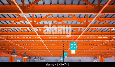 Interior of a warehouse featuring striking orange steel beams and numbered station signs Stock Photo