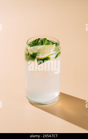 A classic mojito cocktail featuring fresh mint, slices of lemon, and bubbling soda water served in a glass, casting a shadow on a tan background. Stock Photo