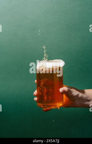 A cropped unrecognizable person's woman's hand confidently holds a glass mug filled with golden light beer, showcasing an overflowing foam head with d Stock Photo