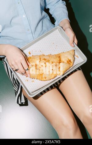 A cropped unrecognizable woman holds a baking sheet featuring a freshly baked cheburek with a crispy, golden-brown crust and melted cheese topping. Stock Photo