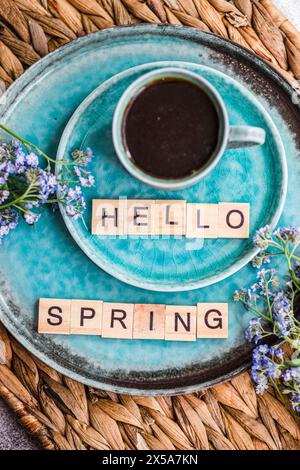 A cup of coffee and forget-me-not flowers on a turquoise plate with Hello Spring spelled out in letter tiles, evoking a fresh springtime mood Stock Photo