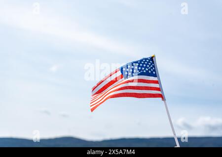 An American flag on a staff, waving in the wind with a clear blue sky and distant mountains as its backdrop, symbolizing USA Independence Day Stock Photo