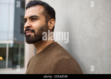 A contemplative man gazes into the distance, his profile captured against the minimalist background of an urban setting Stock Photo