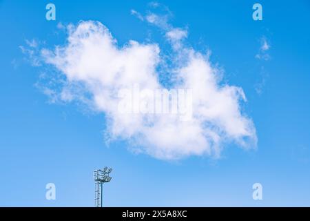 A serene scene depicting puffy cumulus clouds against a vibrant blue sky, with the top of a floodlight pole in view. Stock Photo