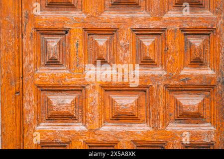 A close-up shot of a vintage wooden door, showcasing textures of peeling orange paint and intricate carved patterns. Stock Photo