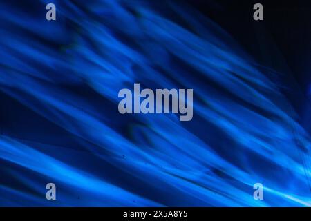 Dynamic blue light rays streak across a dark backdrop in an abstract pattern, symbolizing motion and energy. Stock Photo