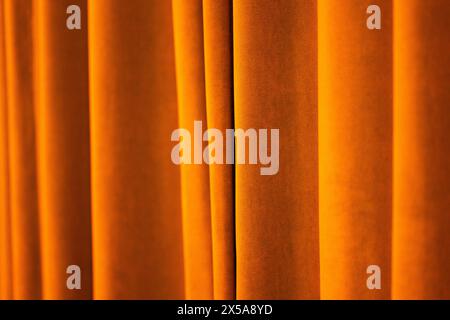 This image captures the luxurious texture of velvet curtains in a warm, golden orange hue, creating a soothing and elegant abstract background. Stock Photo
