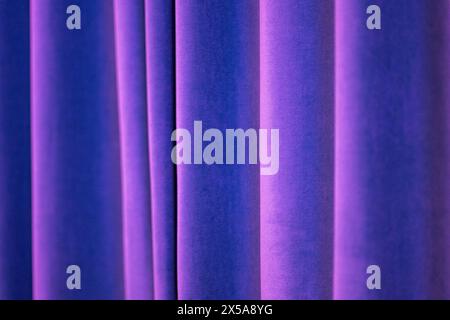A close-up of purple curtains with a smooth texture illuminated by soft, diffused lighting creating a calming abstract pattern. Stock Photo