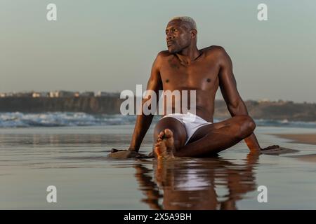 A contemplative African American male model poses on the shore, reflecting in the tranquility of the sunset Stock Photo