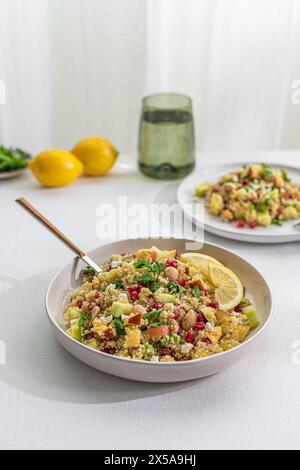 A vibrant quinoa salad mixed with curry spices, fresh vegetables, nuts, and lemon slices, presented in a bowl on a white table, with soft backlighting Stock Photo