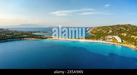 An aerial shot displays the stunning turquoise sea of Rena di Ponente, Sardinia, with a sandy beach, greenery, and buildings nestled among rocky hills Stock Photo