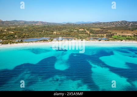 Captivating aerial view showcasing the crystal-clear waters and sandy shores of a tranquil beach in Sardinia, Italy, with lush landscapes in the backg Stock Photo
